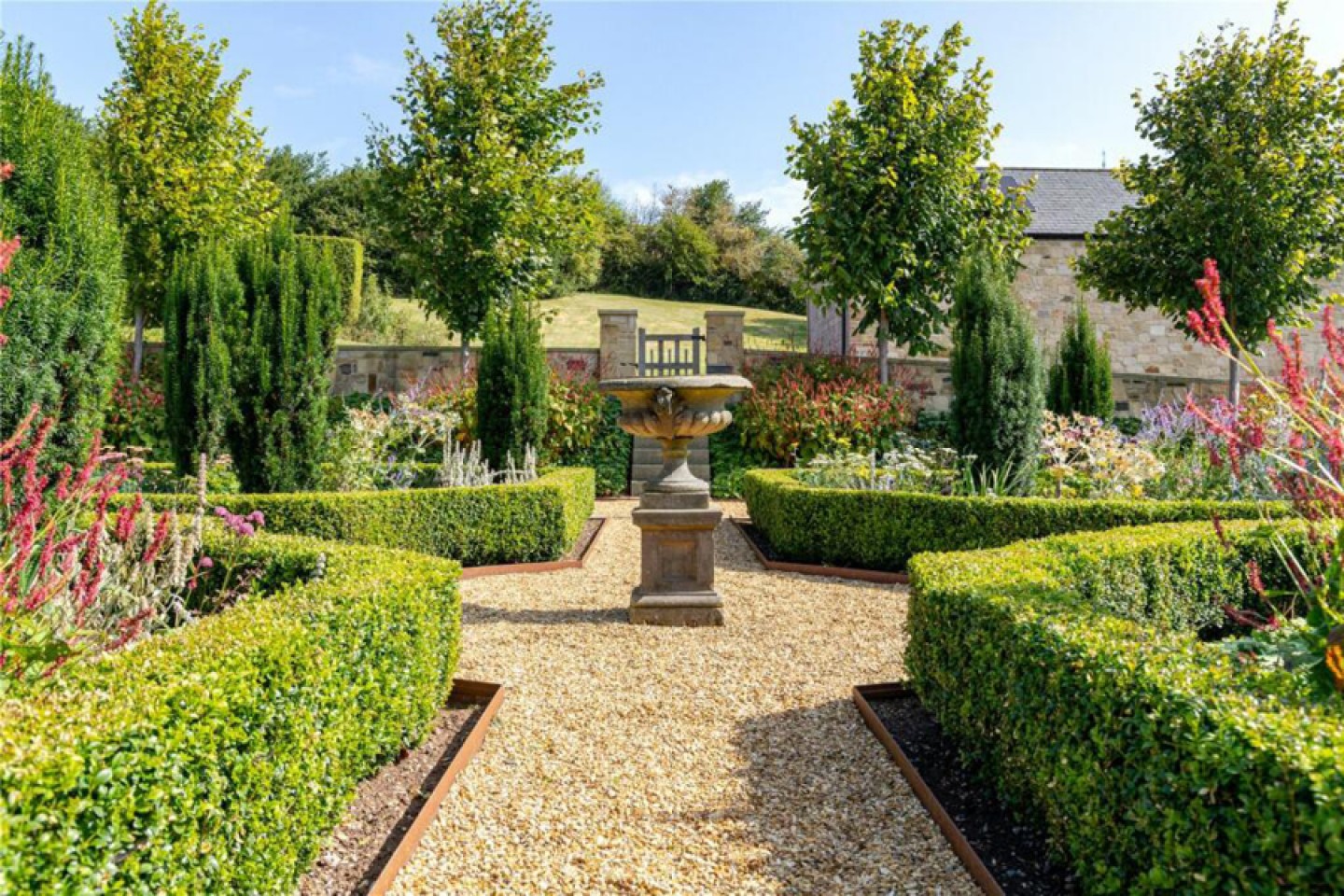 Maintained gravel path lined by low green hedges with a central bird bath